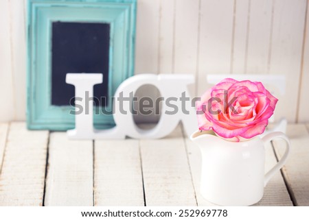 Background with fresh rose and word love.  Rose on white wooden table. Selective focus is on rose.