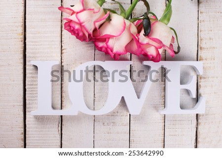 Background with word love  and fresh flowers. Roses on white wooden table. Selective focus is on word.