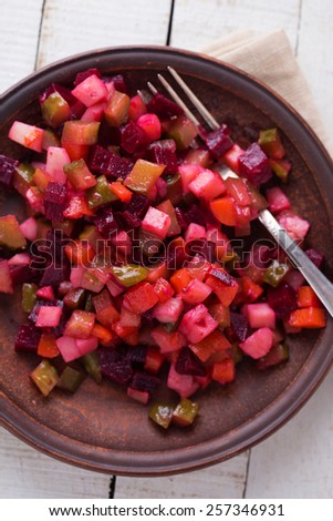 Traditional russian and ukrainian salad with beet, potato, carrot, cucumber on plate on white wooden table. Selective focus.