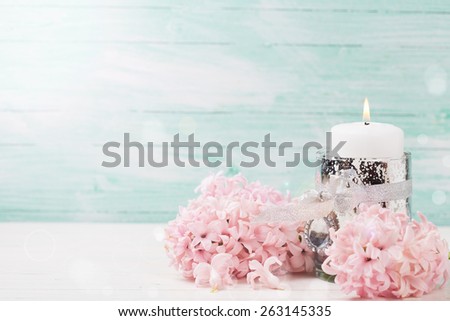 Fresh pink hyacinths flowers and candle on white wooden background against turquoise wall. Selective focus. Romantic background. Place for text.