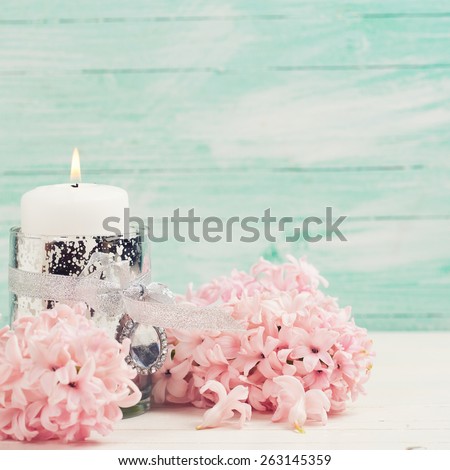 Fresh aromatic hyacinths flowers and candle on white wooden background against turquoise wall. Selective focus. Toned image. Place for text. Square image.
