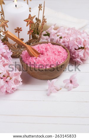 Pink spa  and wellness setting. Sea salt in wooden bowl,  flowers, candle on white painted wooden background. Selective focus. Place for text.
