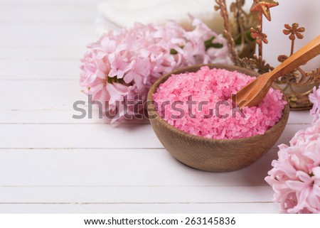 Pink spa  and wellness setting. Sea salt in wooden bowl,  flowers on white wooden background. Selective focus. Place for text.