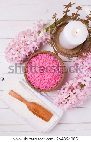 Pink spa  and wellness setting. Sea salt in bowl,  flowers, candle on white painted wooden background. Selective focus. Place for text.