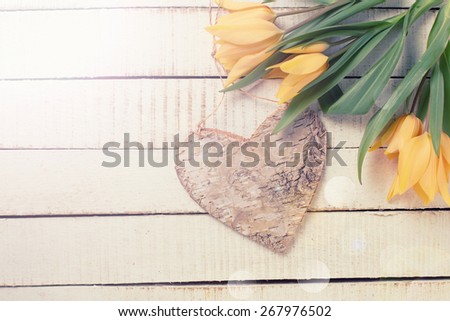 Fresh  spring yellow tulips flowers and decorative heart in ray of light  on white  painted wooden planks. Selective focus. Place for text. Toned image.