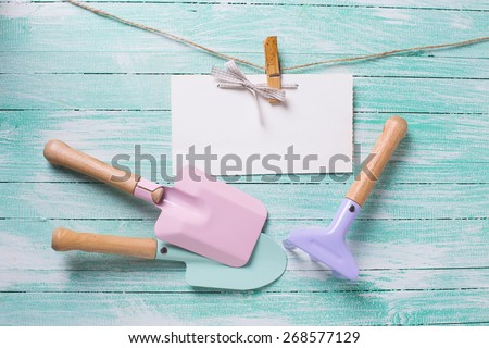 Kids tools for playing in sand and tag on clothes line on turquoise  painted wooden planks. Place for text. Vacation, holiday, summer background.