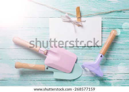 Kids tools for playing in sand and tag on clothes line in ray of light on turquoise  painted wooden planks. Place for text. Vacation, holiday, summer background.