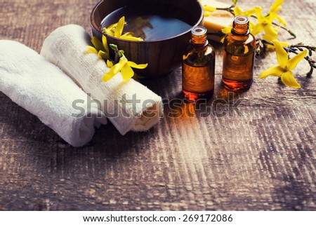 Spa setting. Essential aroma oil , water in bowl, towels, yellow flowers on aged wooden background. Selective focus. Place for text. Toned image.