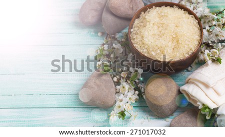 Spa and wellness setting. Sea salt in bowl, towels, stones, flowering branches of trees in ray of light on turquoise painted wooden background. Selective focus.