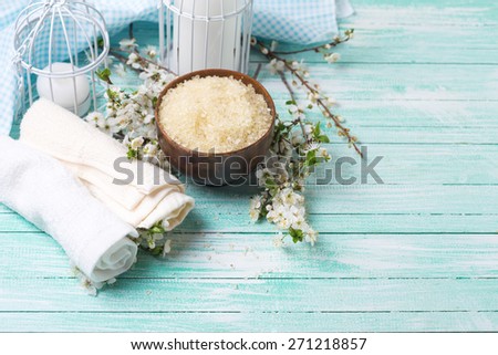 Spa and wellness setting. Sea salt in bowl, towels, candles and  flowering branches of trees on turquoise painted wooden background. Selective focus.