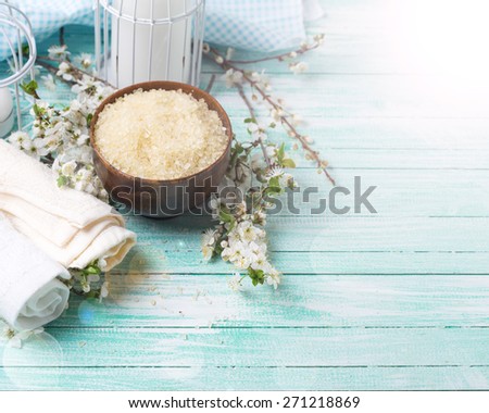 Spa and wellness setting. Sea salt in bowl, towels, candles and  flowering branches of trees in ray of light on turquoise painted wooden background. Selective focus.
