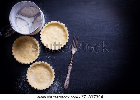 Dough for tarts in tins on black background. Selective focus. Place for text. Toned image.