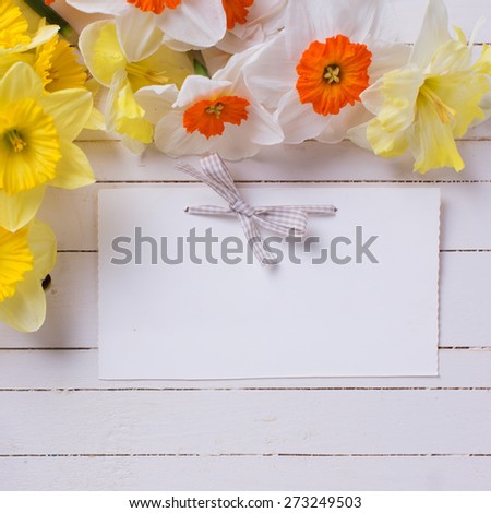 Border from colorful yellow, orange and white spring flowers and empty tag  on white  painted wooden planks. Selective focus. Place for text. Square image.