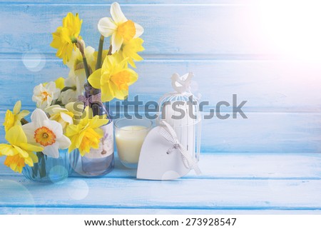 Romantic background. Bright yellow narcissus in vases, candles, heart in ray of light  on blue  painted wooden background. Selective focus. Place for text.