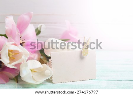 Postcard with fresh spring flowers and empty tag for your text in ray of light on turquoise painted planks against white wall. Selective focus.