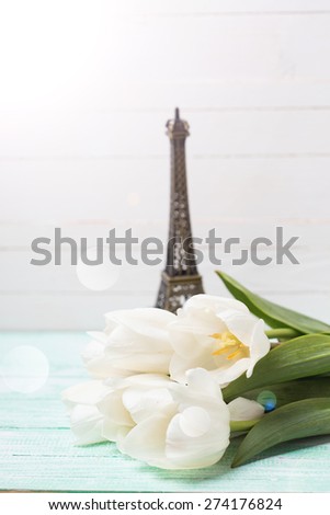 Postcard with fresh spring flowers and little Eiffel tower in ray of light on turquoise painted planks against white wall. Selective focus.