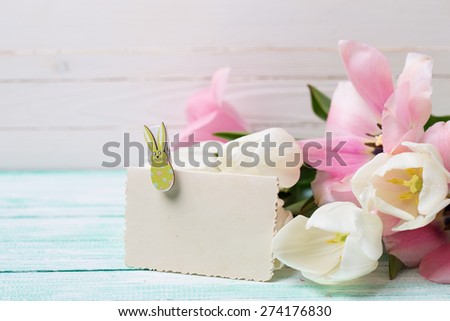 Postcard with fresh spring flowers and empty tag for your text on turquoise painted planks against white wall. Selective focus.