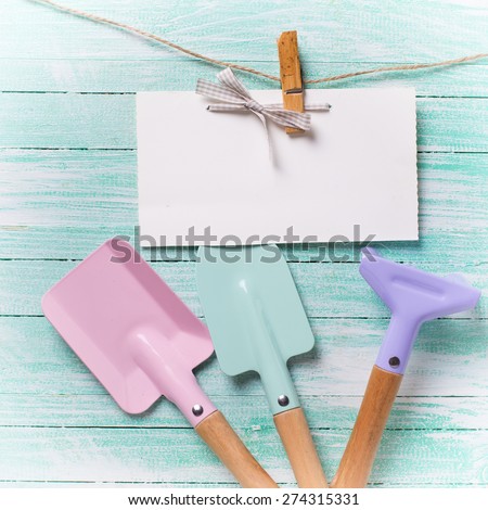Tools for children for playing in sand and tag on clothes line on turquoise  painted wooden planks. Place for text. Vacation, holiday, summer background. Square image.