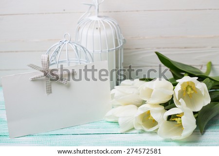Postcard with fresh spring white flowers and empty tag for your text on turquoise painted planks against white wall. Selective focus.