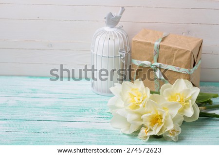 Postcard with fresh  daffodils flowers, candle and gift box on turquoise painted wooden planks. Selective focus. Place for text. Square image.