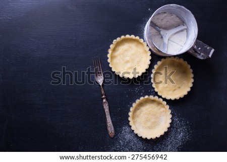 Dough for tarts in tins on black background. Selective focus. Place for text.