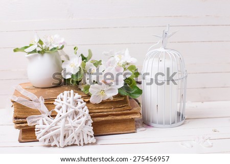 Postcard with tender apple blossom and candle in decorative bird cage in ray of light on white painted wooden planks. Selective focus.