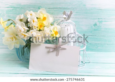Background with colorful narcissus flowers in blue vase, candles  and empty tag for text on turquoise painted wooden planks. Selective focus. Place for text. Toned image.