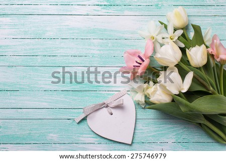 Fresh  spring yellow tulips and narcissus flowers and decorative heart on turquoise  painted wooden background. Selective focus. Place for text.