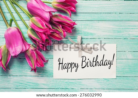 Fresh pink  tulips and  tag with phrase Happy Birthday on it  on turquoise  painted wooden background. Selective focus. Place for text.