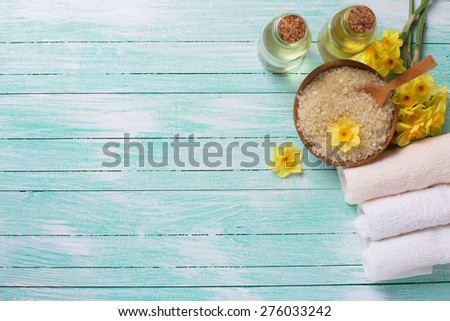 Spa or wellness setting. Sea salt in bow, aroma oil, towels and yellow flowers on turquoise painted wooden background. Selective focus. Place for text.