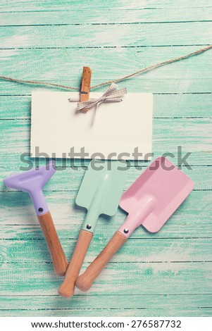 Tools for children for playing in sand and tag on clothes line on turquoise  painted wooden planks. Place for text. Vacation, holiday, summer background. Toned image.