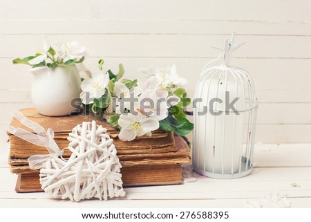 Postcard with apple blossom, decorative heart, old books and candle in decorative bird cage on white painted wooden planks. Selective focus. Toned image.