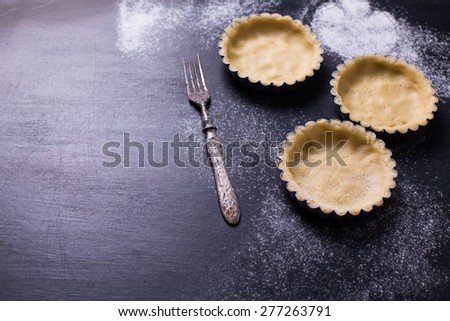 Dough for tarts in tins on black background. Selective focus. Place for text.