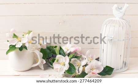 Postcard with tender apple blossom and candle in decorative bird cage on white painted wooden background. Selective focus. Toned image.