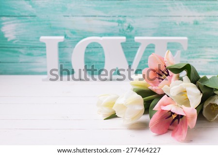Fresh  white and pink tulips flowers and word love on white  painted wooden background against turquoise wall. Selective focus. Place for text.