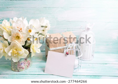 Background with colorful narcissus flowers , candles, box with present  and empty tag for text in ray of light on turquoise painted wooden planks. Selective focus. Place for text.