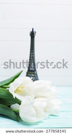 Postcard with fresh spring flowers and little Eiffel tower on turquoise painted planks against white wall. Selective focus. Toned image.