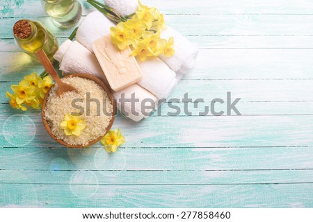 Spa or wellness setting. Natural sea salt in  wooden bow, organic soap, aroma oil, towels and yellow flowers  in ray of light on turquoise painted wooden background. Selective focus. Place for text.