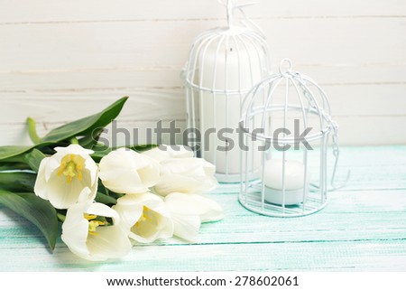 Background with fresh spring flowers and candles in decorative bird cages on turquoise painted planks against white wall. Selective focus. Toned image.