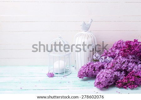 Background  with fresh lilac flowers and candles in decorative bird cages  on turquoise painted wooden planks against white wall. Selective focus. Place for text.
