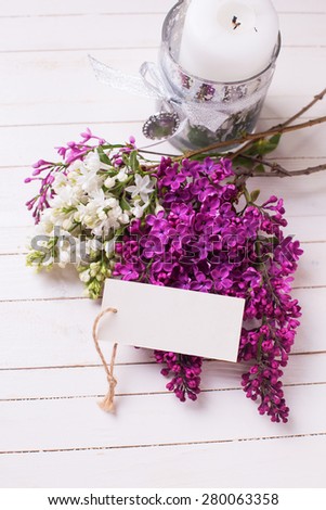Postcard with fresh white and violet lilac flowers on white painted wooden planks. Selective focus. Place for text on empty tag.