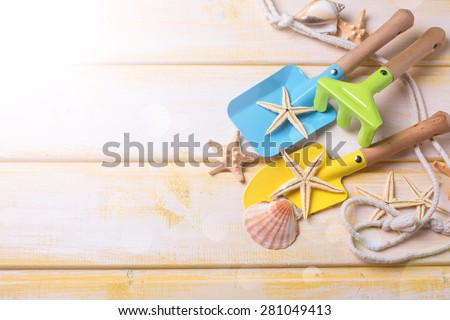Tools for kids for playing in sand and sea object in ray of light on  yellow  painted wooden background. Place for text. Vacation background.