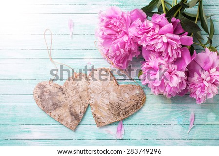Wedding background. Splendid  pink  peonies flowers and two decorative hearts in ray of light  on turquoise painted wooden planks. Selective focus is on flowers.