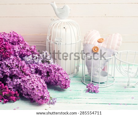 Background  with fresh lilac flowers, candle in decorative bird cage and decorative  heart   on turquoise painted wooden planks against white wall. Selective focus. Place for text. Toned image.