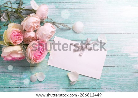 Postcard with fresh roses flowers and empty tag for your text in ray of light on turquoise painted wooden background. Selective focus.