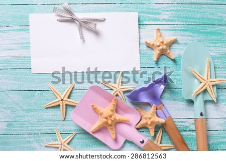 Empty tag and tools for children for playing in sand, sea object on turquoise  painted wooden planks. Place for text. Vacation, holiday, summer background.