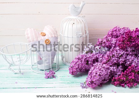 Background  with fresh lilac flowers, candle in decorative bird cage and decorative  heart   on turquoise painted wooden planks against white wall. Selective focus. Place for text.