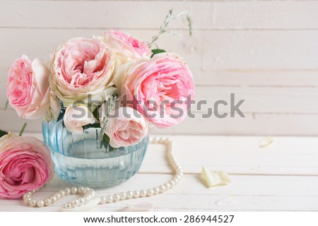 Background with sweet pink roses flowers  in blue vase on white painted wooden background. Selective focus. Place for text. Toned image.
