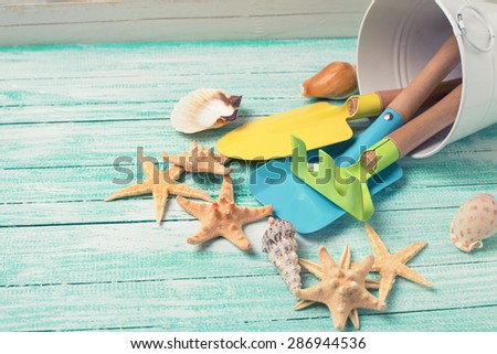 Tools for kids for playing in sand and sea objects on turquoise  painted wooden planks. Place for text. Vacation background. Toned image.
