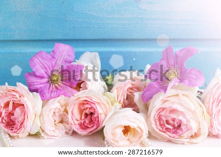 Pastel pink roses, clematis flowers  in ray of light on white wooden background against blue wall. Place for text. Selective focus.